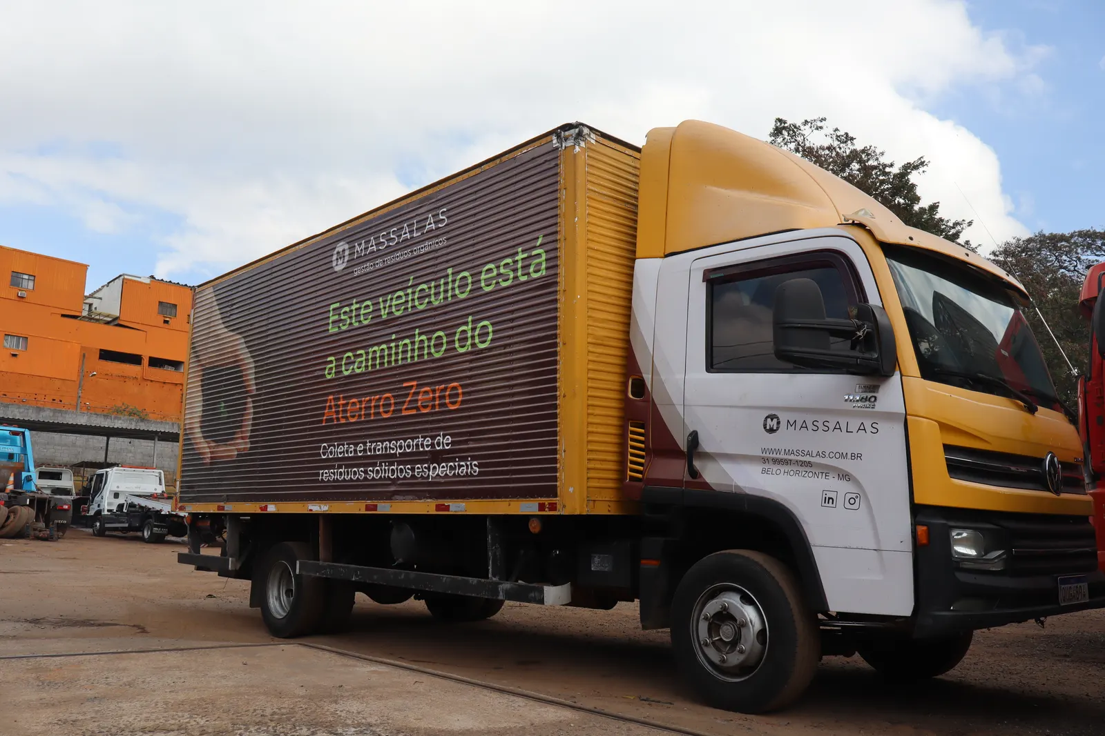 Caminhão baú da Massalas visto de frente, com a cabine amarela e a plotagem da marca na lateral.