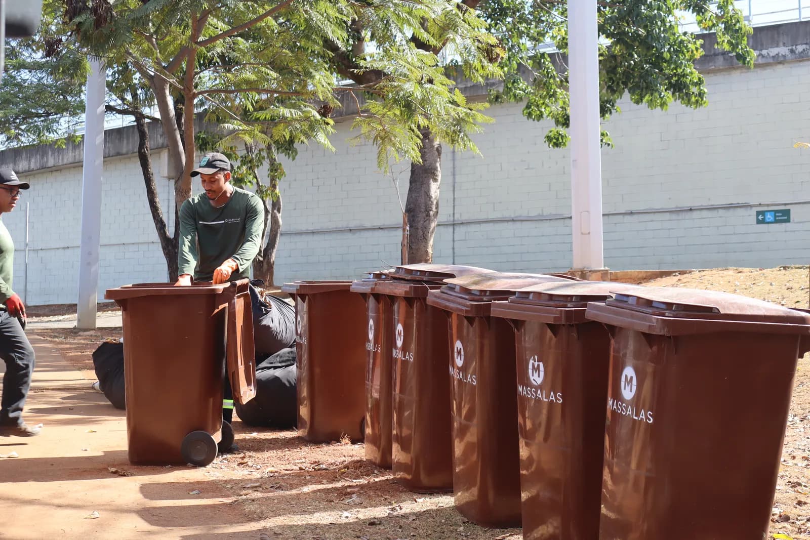 Operador da Massalas manejando contentores marrons no pátio arborizado de um cliente.